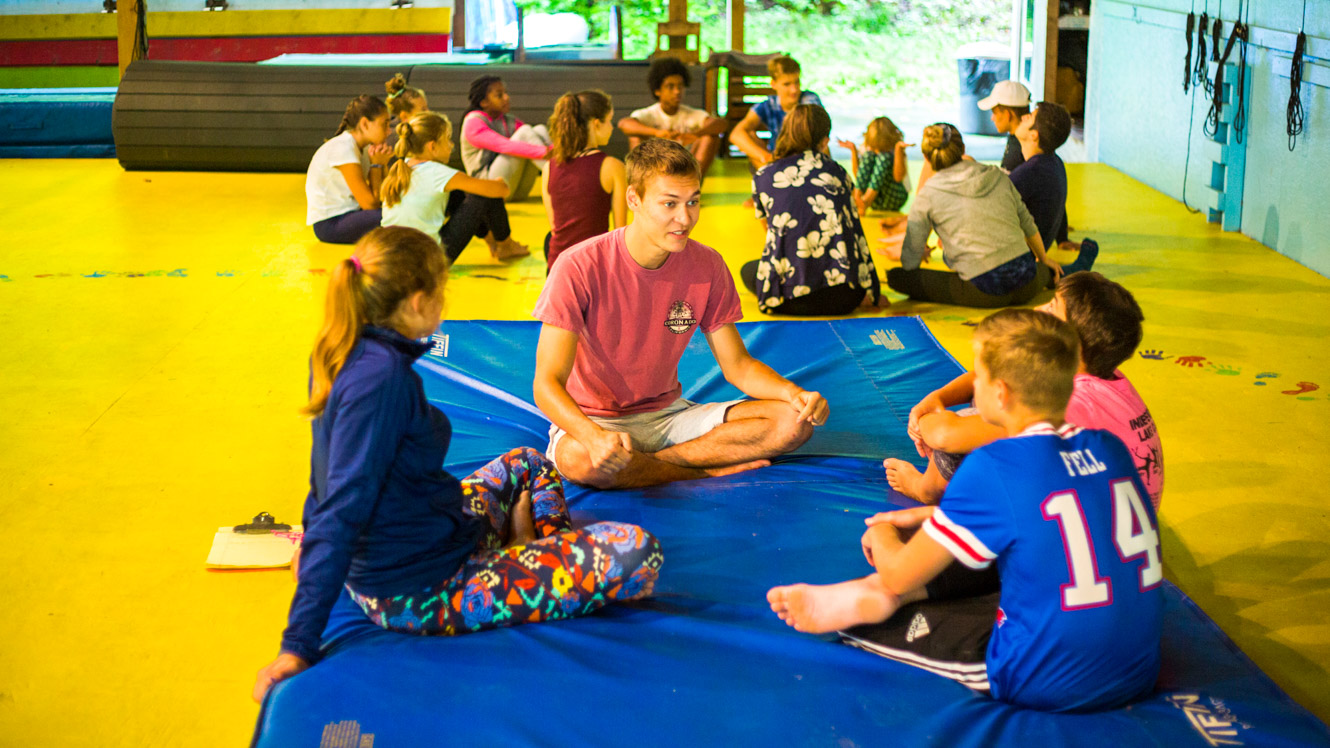 Staff member sits with campers on mat